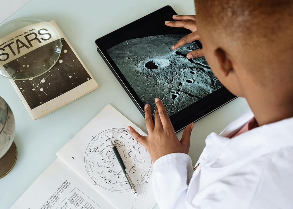 Photo of an African American student studying craters of moon on tablet at observatory.